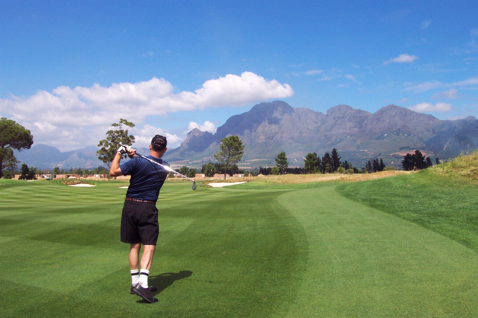 Golfer teeing off on a South African course with mountains beyond, combining golf and safari